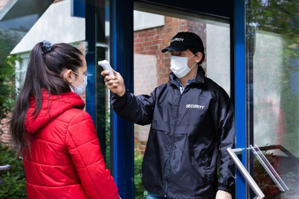 Security officer checking temperatures of people before entry.